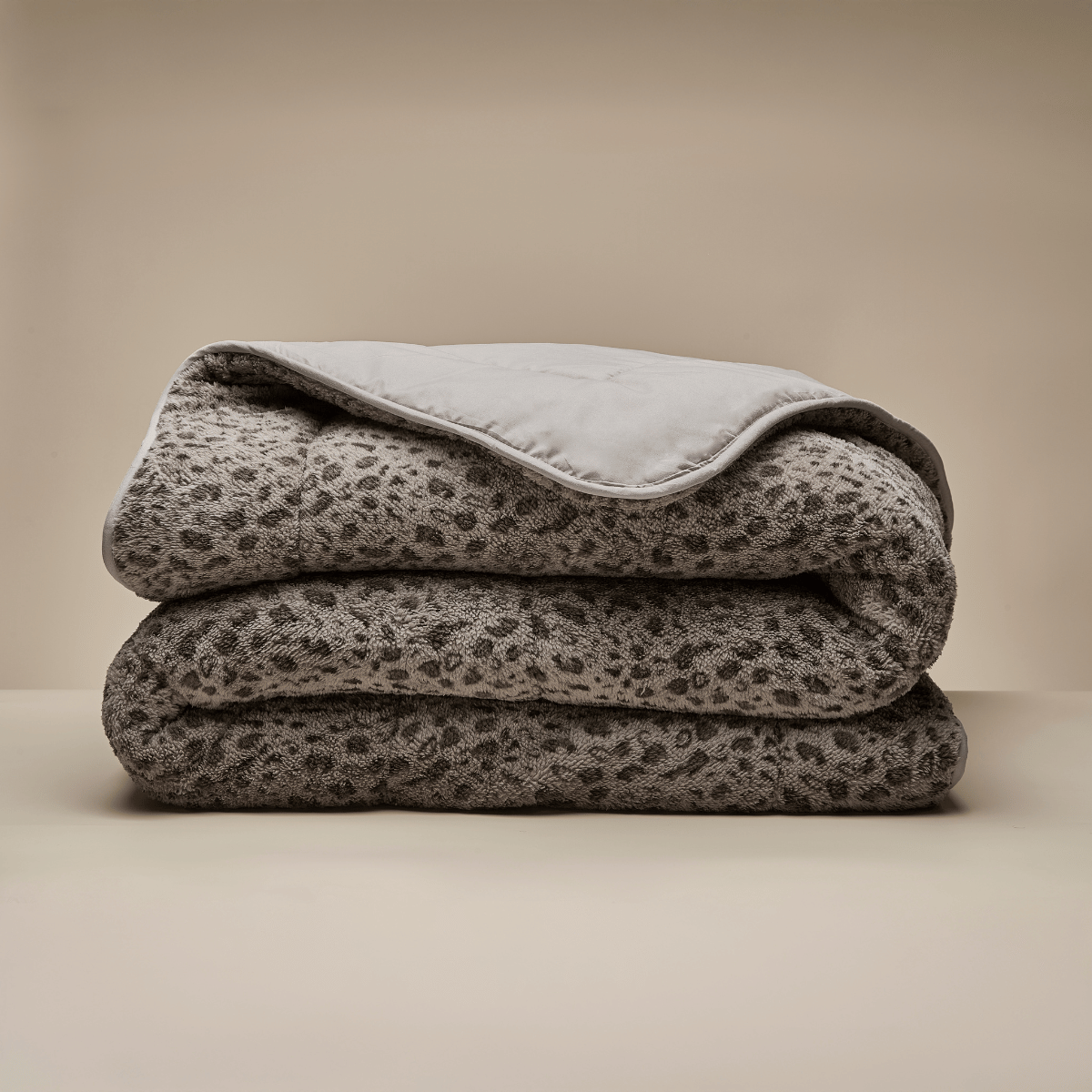 The Zelesta Teddybed - Panther Taupe is a plush, folded blanket featuring a grey and black leopard print, displayed on a neutral surface with a beige background—ideal for those who love cozy teddy duvets.