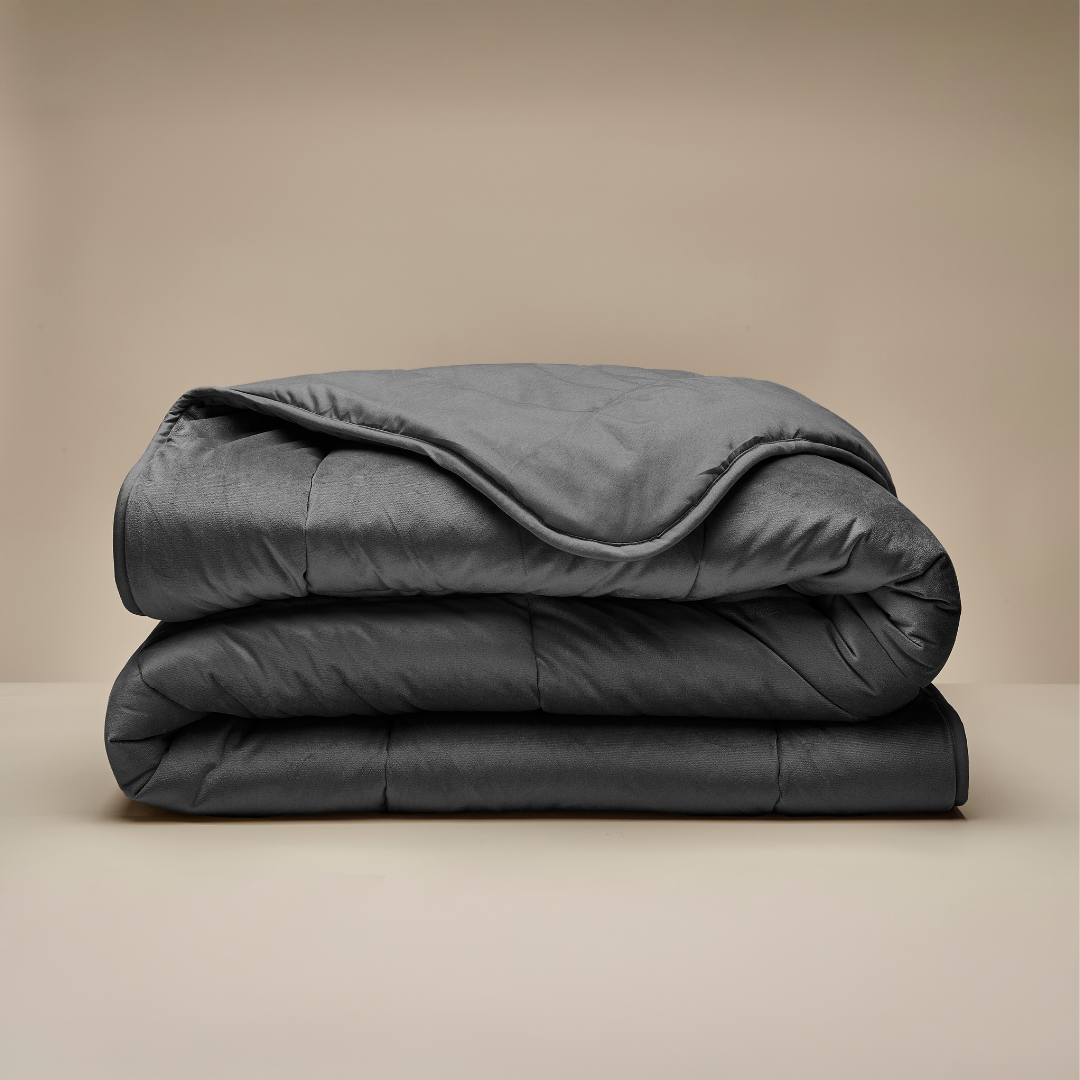 The Zelesta Velvetbed - Anthracite, a neatly folded dark gray washable velvet duvet, is stacked on a light beige surface with a neutral beige background.
